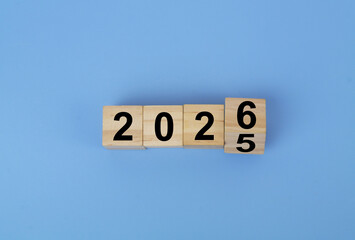 Wooden cubes with flipping numbers 2025 and 2026 on blue background. New year and new changes concept.